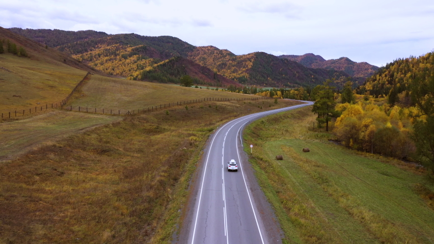 4K Aerial drone footage of small white family hatchback moving through picturesque landscape. car driving on an asphalt road with a beautiful mountainous terrain. | Shutterstock HD Video #1076145185