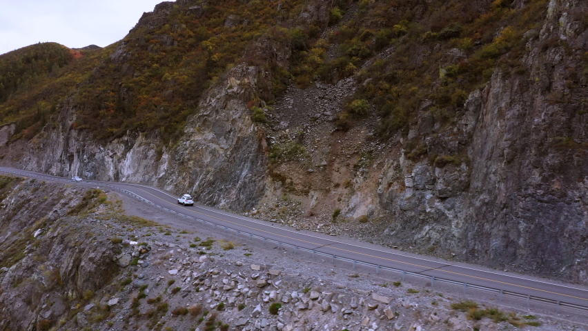 Aerial frame. A white car with a roof rack drives on an asphalt road along a mountain serpentine. Hedgeback road trip in a picturesque mountainous area. | Shutterstock HD Video #1076145200