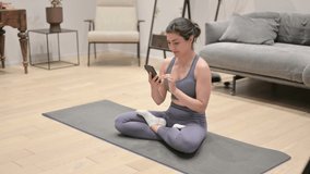 Indian Woman Talking on Video Call on Smartphone while Sitting on Yoga Mat 
