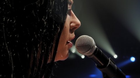 Portrait of a beautiful singer with long hair on a dark stage in the spotlight.