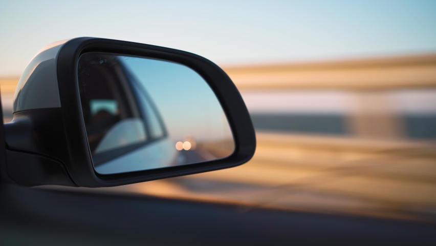View in the side mirror of a car that is driving fast on the highway in the sunset light. Travel and trip concept. Royalty-Free Stock Footage #1076154170