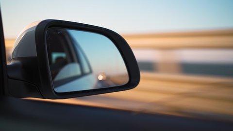 View in the side mirror of a car that is driving fast on the highway in the sunset light. Travel and trip concept.