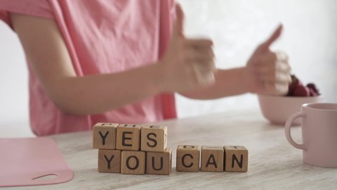 Motivating quote YES YOU CAN on table. Woman makes a joyful positive gesture with her hands. Clenched fists with thumbs up. Сoncept of success, setting goals and achieving them. Motivation
