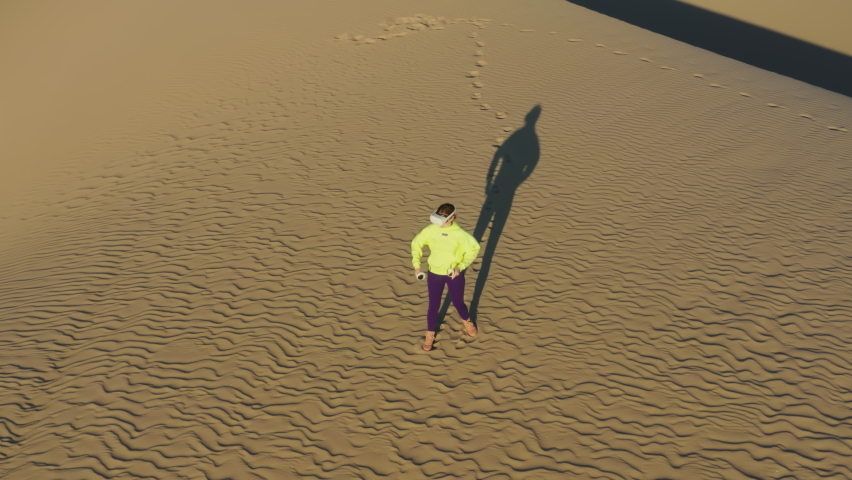 Young woman in sportswear doing sports, playing archery video game in nature park at sunset. Active athletic female in VR glasses training in virtual reality outdoors on sand dunes. Technology concept