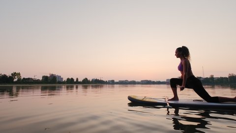 Young woman doing yoga on SUP board at sunset. Slow motion futage