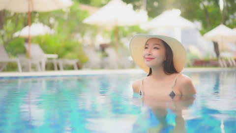 Dreamy scene with beautiful happy asian woman in swimming pool with floppy hat, full frame slow motion