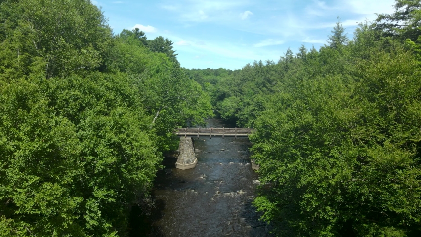 Beautiful scenic birds-eye view flying over the river and under the bridge on a sunny day.