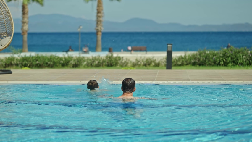 A young woman wearing a hijab swimsuit is swimming in the pool with her husband and young son. Happy young couple having fun in the pool with their son. A happy family is enjoying their vacation. 