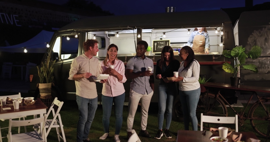 Multiracial people talking in front of food truck outdoor - Multigeneratiol friends having fun eating dinner outside at summer time 