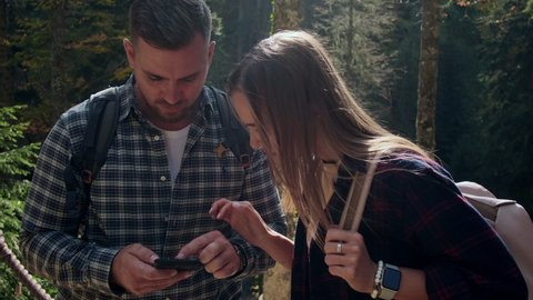 male and female backpackers are viewing electronic map in smartphone, walking in natural park, pair of hikers walking in woodland, orienting by app in cell phone