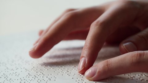 Touching letters on sheet of paper close-up, blindman reading braille book using his fingers, poorly seeing person learning to read, disabled people concept. 