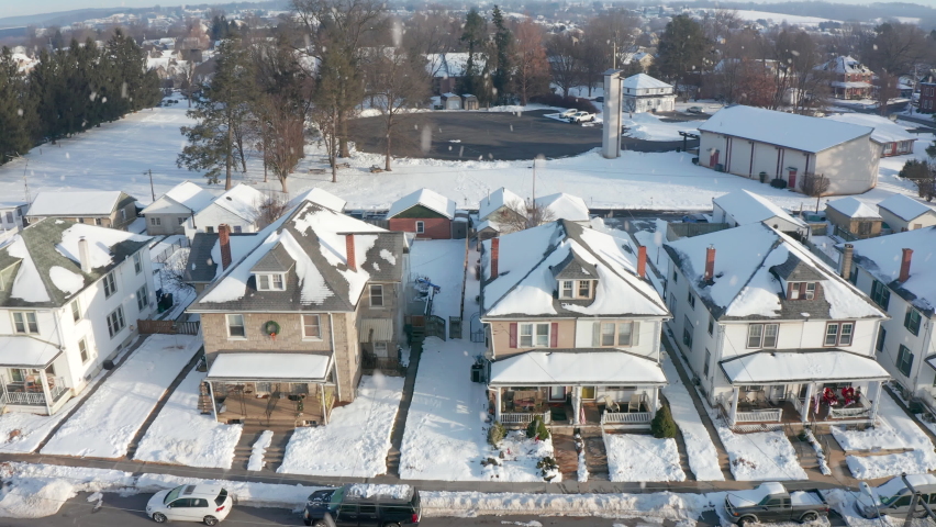 It's Snowing. American homes decorated for winter Christmas. Snowflakes falling from sky. Aerial establishing shot of houses along USA street in town.