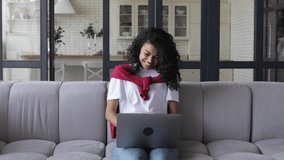 Young afro american woman student or freelancer with curly hair, working or studying remotely at home using laptop computer for video call, talking at an online meeting with colleagues