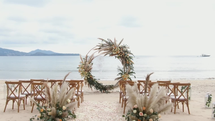 Wedding decor beach set up seaside floral roses arch sunny summer Germany. Best Wedding Western details Wood chairs gold concept. Setting stage festive marriage patterns tropical island sunset.  | Shutterstock HD Video #1076171981