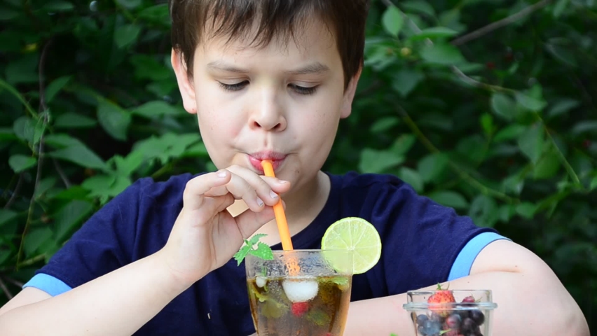 Child boy drinks natural lemonade summer drink, tea with wild berries, lime, raspberries and blueberries, summer vacation in park. refreshing natural drink lemonade Detox fruit infused water cocktail