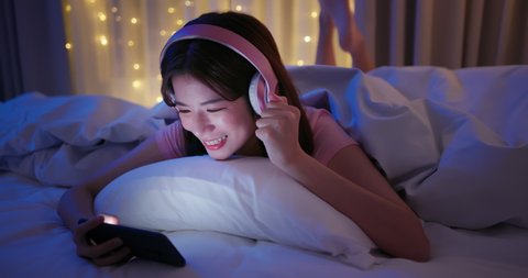 asian woman wearing headsets play mobile games and win with fist gesture by smartphone on bed at night