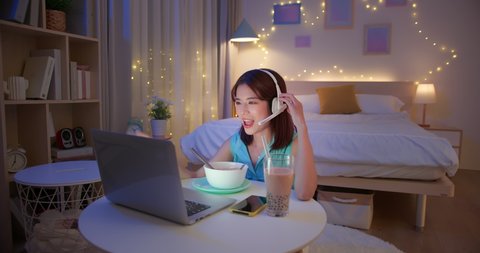 asian woman is eating instant noodles and tapioca ball milk tea while having video meeting on laptop computer at home in the evening
