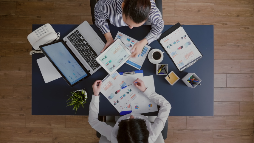 Top view of business women comparing financial graphs with management statistics expertise discussing company strategy working in startup office. Corporate directors brainstorming economy ideas, a Business & Finance Video by DC Studio