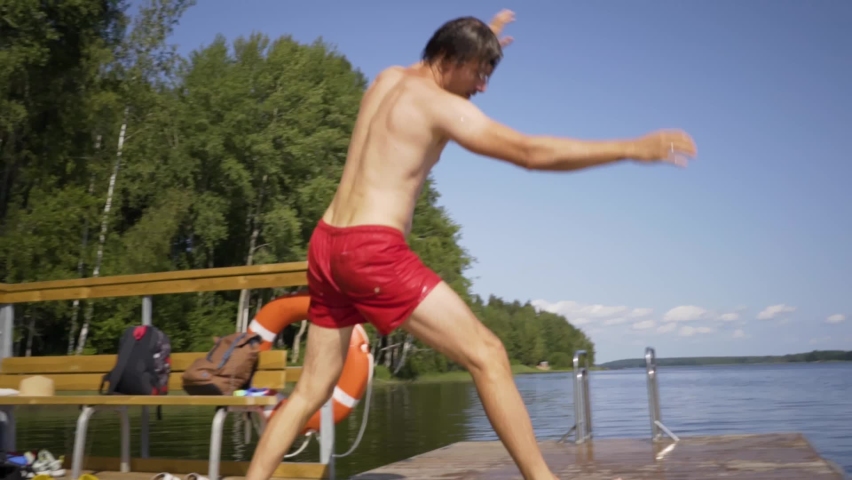 Young man jumping into the lake from wooden pier. Having fun on summer day. Man diving in to the water.