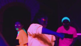Group of female and male stylish dancers dancing inside dark place with neon lights .  Beautiful young people with fluorescent colorful make-up and clothes dancing in UV light. HD video in slow motion