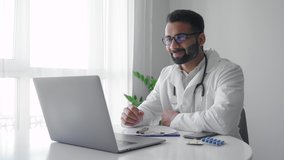 Middle age adult indian man physician doctor wearing white coat video calling distant patient on laptop. Professional medical specialist talking to client using virtual chat computer app. Telemedicine