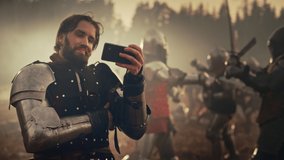 Portrait of Handsome Medieval Knight Using Smartphone Horizontally on Battlefield, Smiling. Armored Warrior Watching Online Gaming, Streaming on Demand Funny Videos. In Background War is Raging
