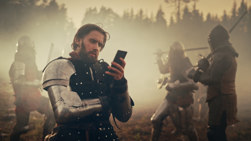 Portrait of Handsome Medieval Knight Using Smartphone on Battlefield, Smiling. Funny Concept: Armored Warrior Having Fun, Ordering Online, Betting, Investing, doing E-commerce. War is Raging | Shutterstock HD Video #1076193317