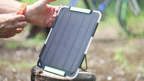 Man connecting smartwatch to portable solar panel to charge from sunlight. Charging watch from renewable energy.