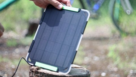  Man setting portable solar panel to charge watch from sunlight. Charging watch from renewable energy.