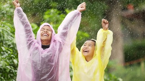 Portrait of Funny boy and girl wears raincoat and put they hand in rain. Happy asian brother and sister enjoying the rain dressed in garden. Cheerful, excited boy and girl having fun, wet under rain.