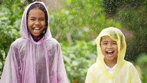 Portrait of Funny boy and girl wears raincoat in rain. Happy asian brother and sister enjoying the rain dressed in garden. Cheerful, excited boy and girl having fun, wet under rain.