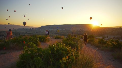 Goreme, Cappadocia, Turkey - May 30, 2021: Ballooning in Kapadokya. Many people waiting on top of hill to watch hot air balloons flying over valleys in blue sunrise morning sky and to take photoes