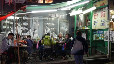 HONG KONG CIRCA MARCH 2017, night street restaurant close view, people at tables eating Cantonese food, one woman outside looking into restaurant, passers by, Central Mid Levels