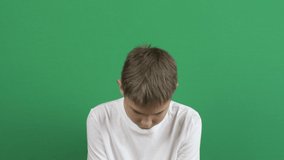 Upset disappointed depressed teenage boy sitting lowered his head, raises and lowers his head sadly. Emotions, problems, depression. Green screen chroma key background. 4k video