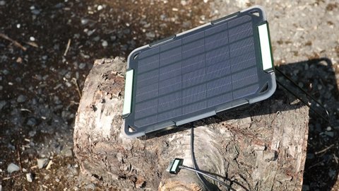 Close up on hand connecting tablet to portable solar panel to charge from sunlight. Charging watch from renewable energy.