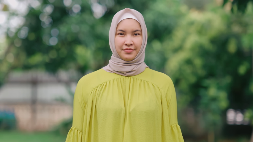 A beautiful middle-aged Asian Muslim woman. Standing smiling and raising hands to greet the camera with bright cuteness at the garden