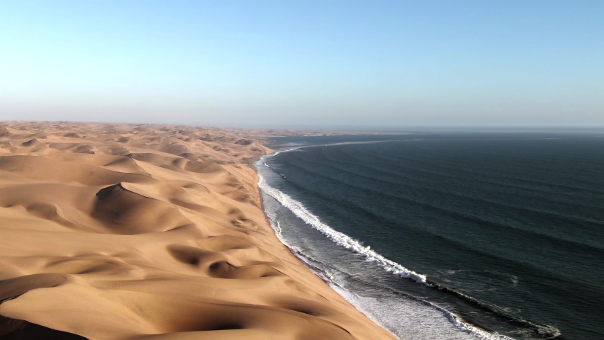 Aerial view of Sandwich Harbour, where towering sand dunes meet the Atlantic coast, near Walvis Bay in the Namib-Naukluft National Park, Namibia. Royalty-Free Stock Footage #1076205638