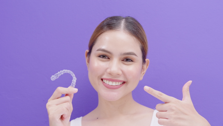 Young smiling woman holding Invisalign braces in studio, dental healthcare and Orthodontic concept.	 | Shutterstock HD Video #1076208284