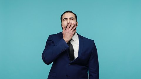 Drowsy tired bearded man in formal suit need rest, yawning wide feeling sleepy exhausted, difficult wake up, having insomnia chronic fatigue syndrome. Indoor studio shot isolated on blue background.