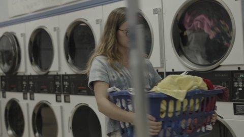 Girl carrying laundry basket in laundromat and reading book  Provo, Utah, United States