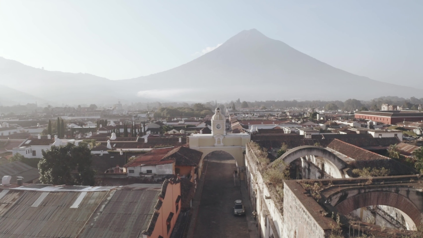 Aerial view of sunrise in Antigua Guatemala with Agua volcano behind - Arch of Santa Catalina in Antigua Guatemala seen from above early in the morning Royalty-Free Stock Footage #1076211836