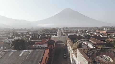 Aerial view of sunrise in Antigua Guatemala with Agua volcano behind - Arch of Santa Catalina in Antigua Guatemala seen from above early in the morning