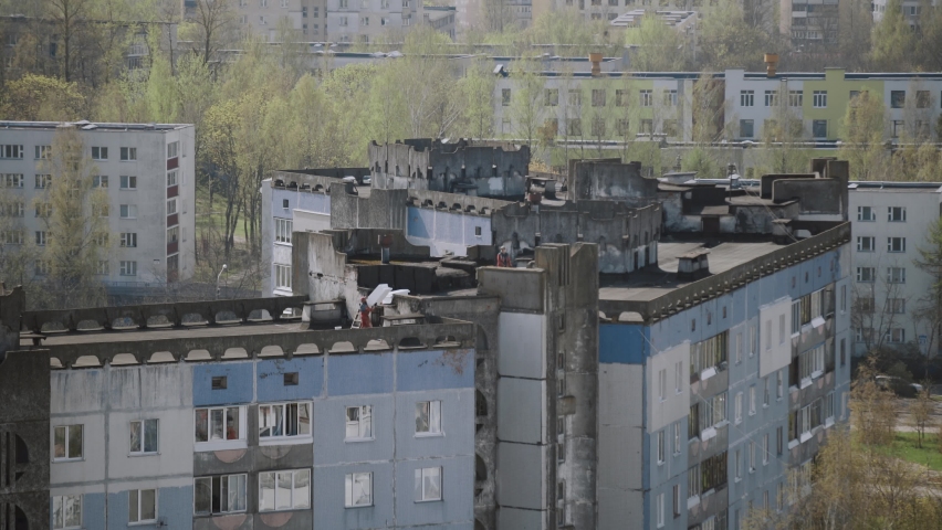 Two workers carry white sheets of insulation on the roof of multi-storey building. Warming of old concrete panel houses in the city.