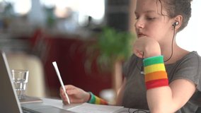 Young girl is talking on video communication at home using wired headphones. On the rock, the girl has a wristband with lgbt symbols