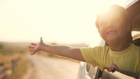 Child in car window. Family car trip. Child hair in wind. Girl looks out of car window. Happy child travel with his family. Girl stretches out his hand to wind. Happy family travel concept by car