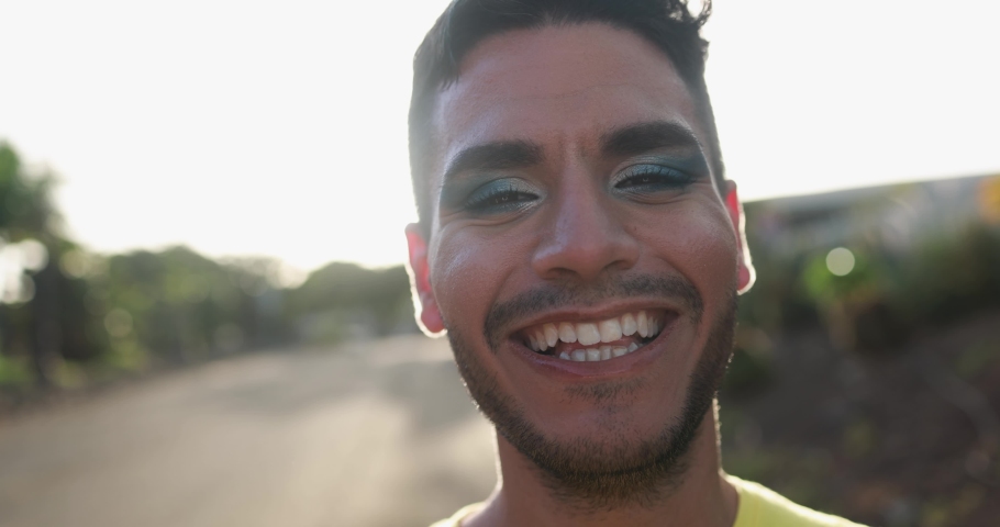 Young transgender man with makeup smiling on camera with sunset in the background