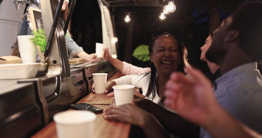 Multiracial people talking together  in front of food truck outdoor - Multigeneratiol friends having fun eating dinner outside at summer time 