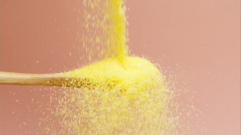 Falling polenta on wood spoon on pink background close-up. Shooting of cereal and groats in studio. Macro footage of pouring out the grits. Food cooking, harvest video. 