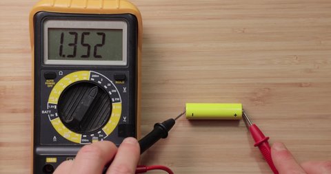 Testing AA battery cell with digital multimeter tool, voltage check showing low value, battery is used and mostly discharged