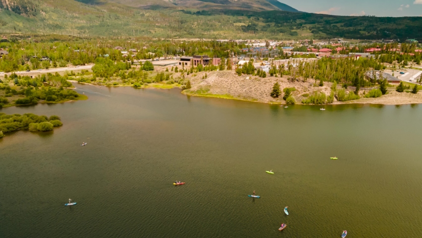 Canoes, kayaks, and paddle boards on Dillon Reservoir with the mountains and Frisco, Colorado in the background, cloudscape overhead aerial hyper lapse